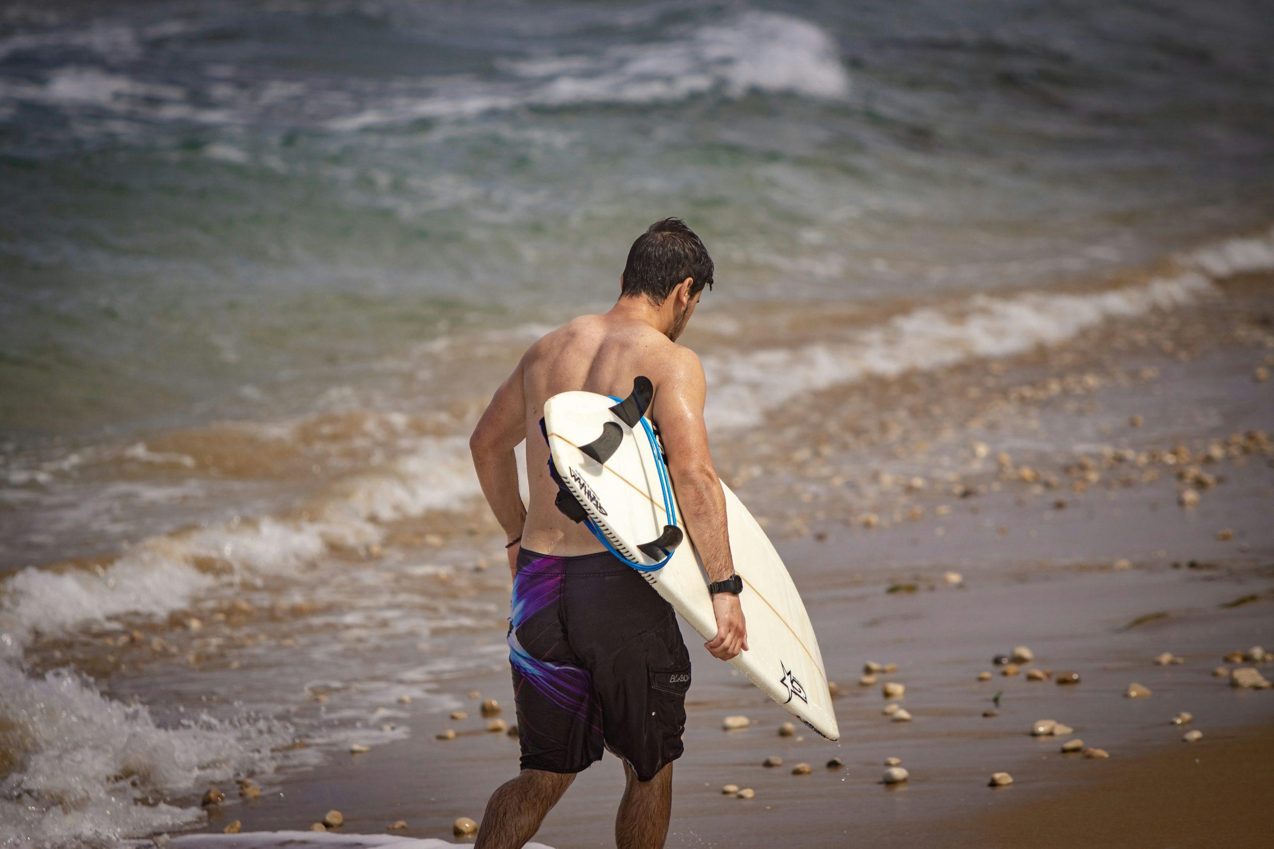 A surfer holding his clean, well-maintained surfboard luggage at the beach.