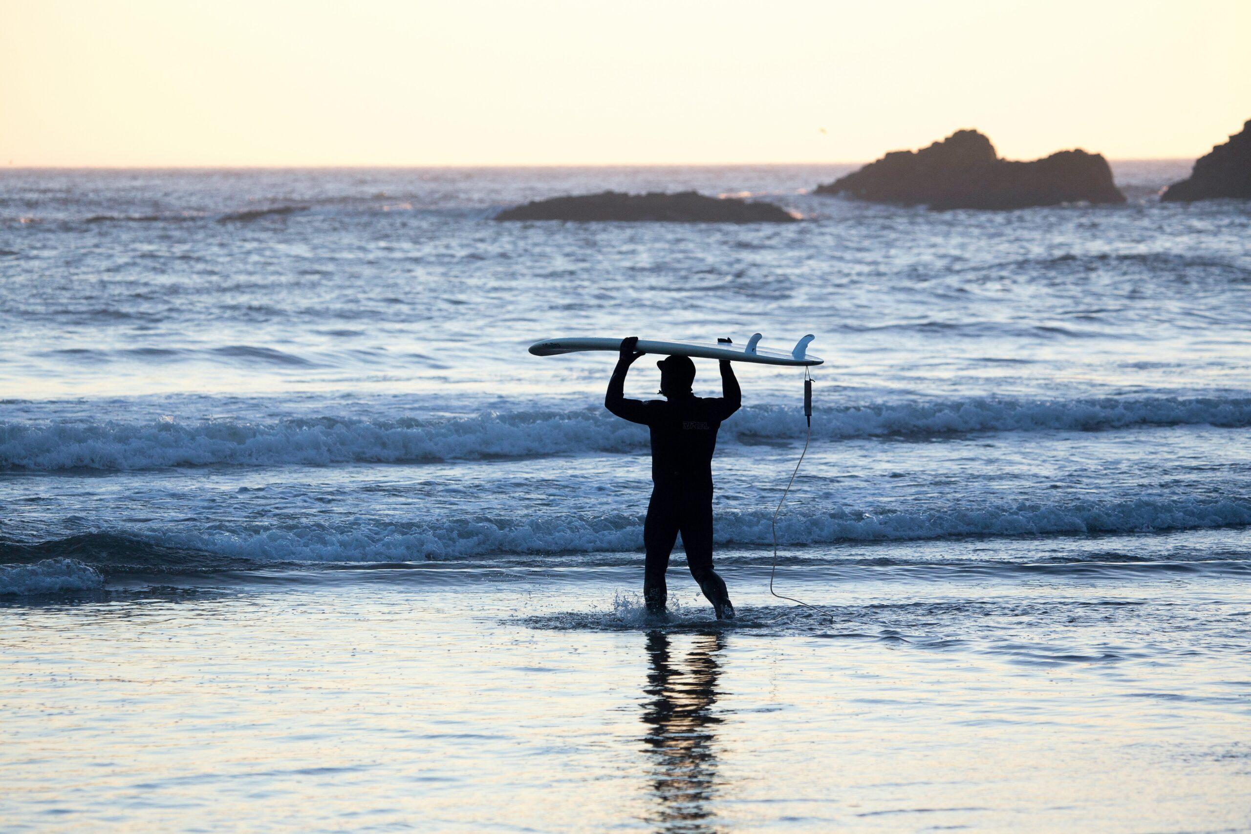 Happy traveler holding surfboard next to ocean waves