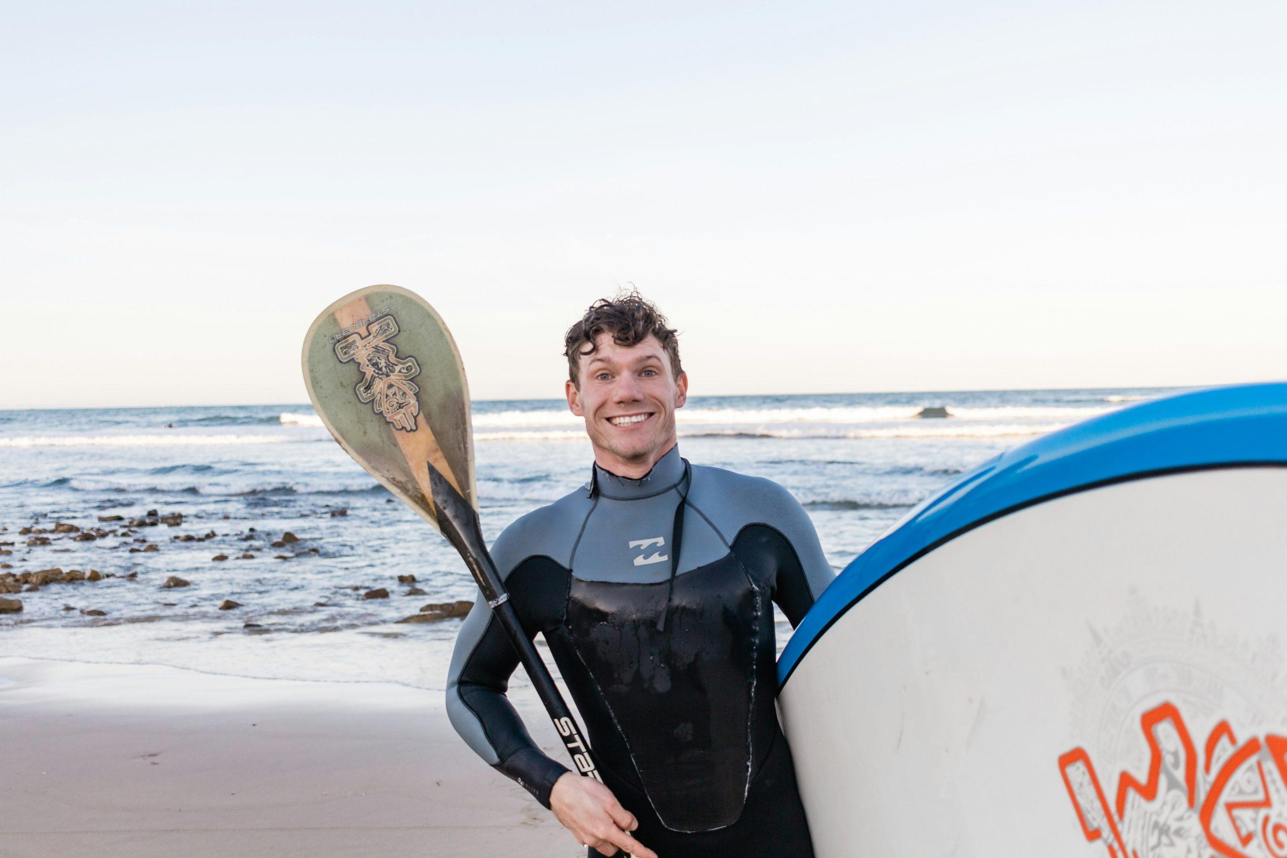 Smiling surfer holding surfboard near beach