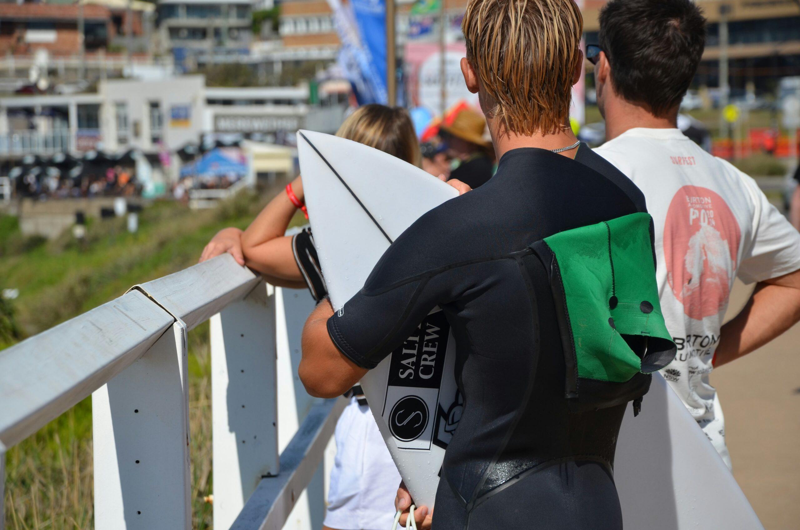 A smiling surfer holding his surfboard at an airport check-in counter