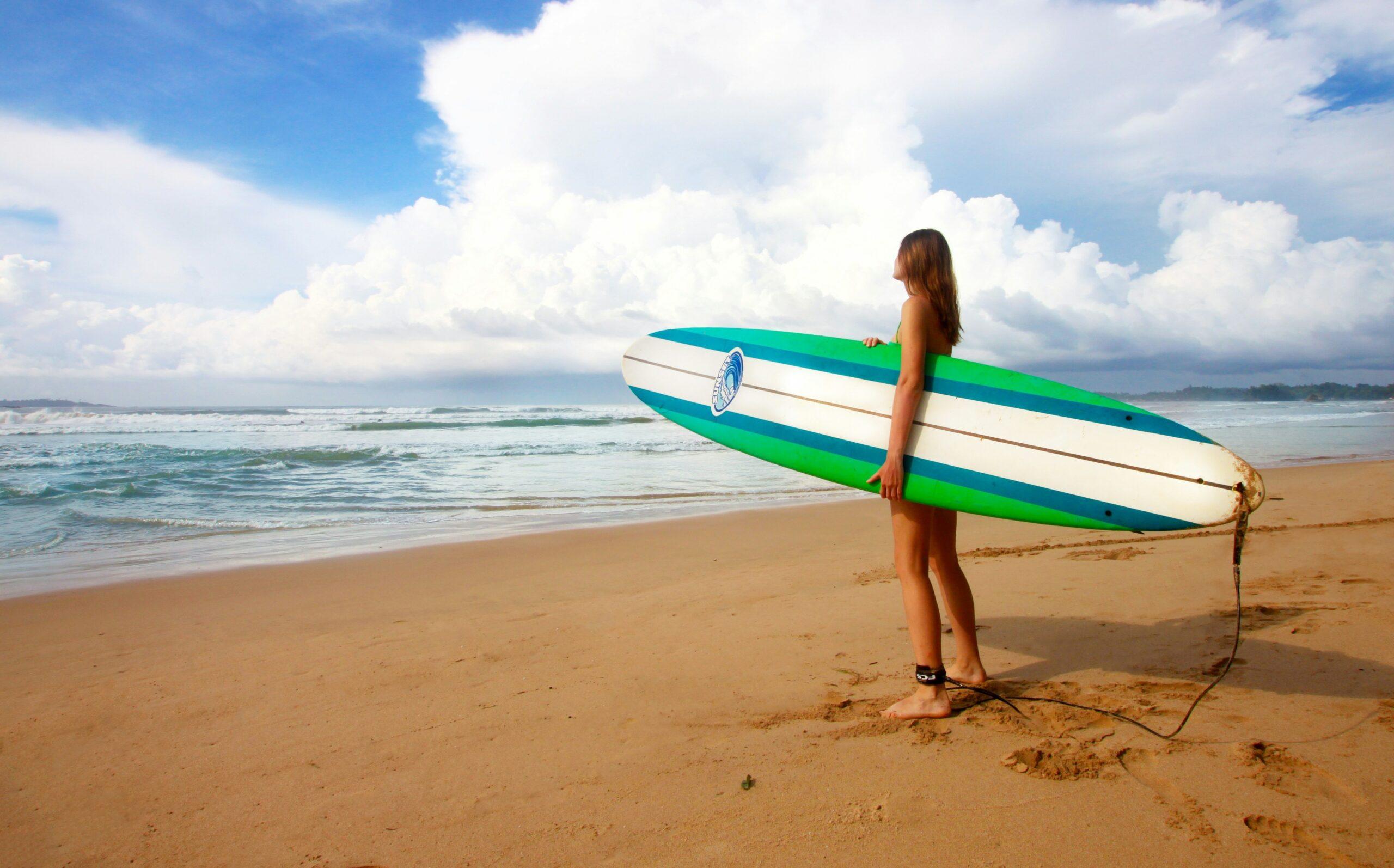 Maria holding her foldable surfboard case at a beachside airport terminal.