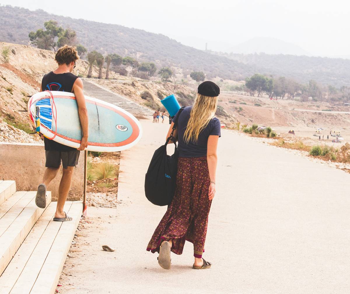 A professional female surfer holding her heavily padded surf transport bag near the ocean.