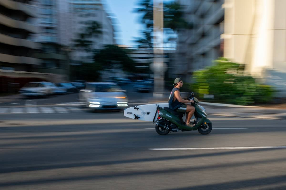 A man carrying a surfboard inside a padded travel bag at the beach.